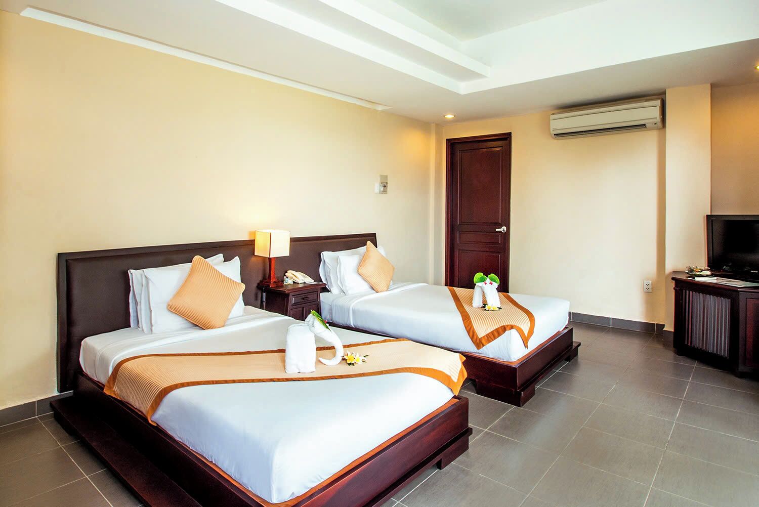 A hotel room with two beds, a TV, and an air conditioning unit.