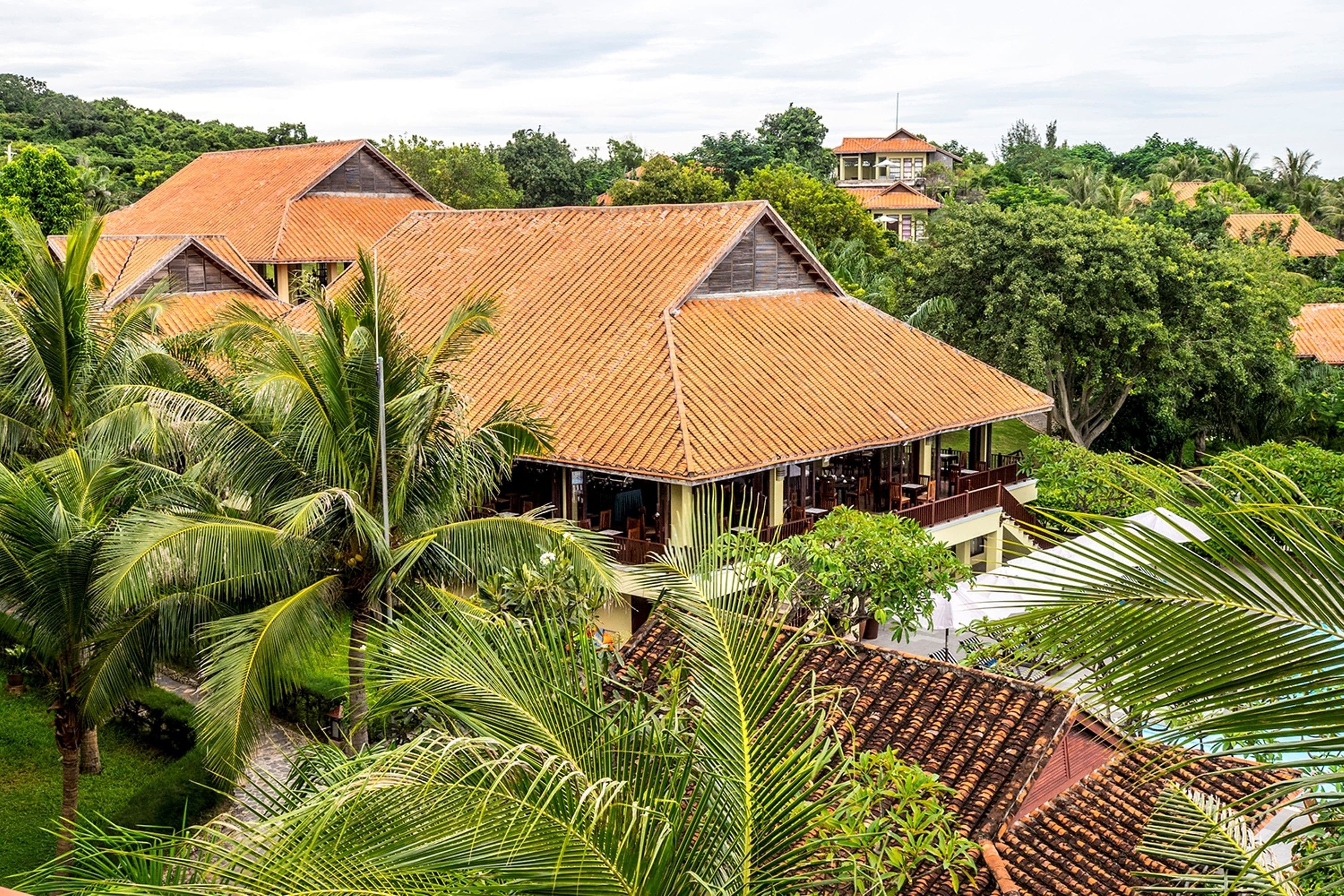 Ein tropisches Resort mit mehreren Gebäuden und roten Ziegeldächern, umgeben von üppiger Vegetation und Palmen.