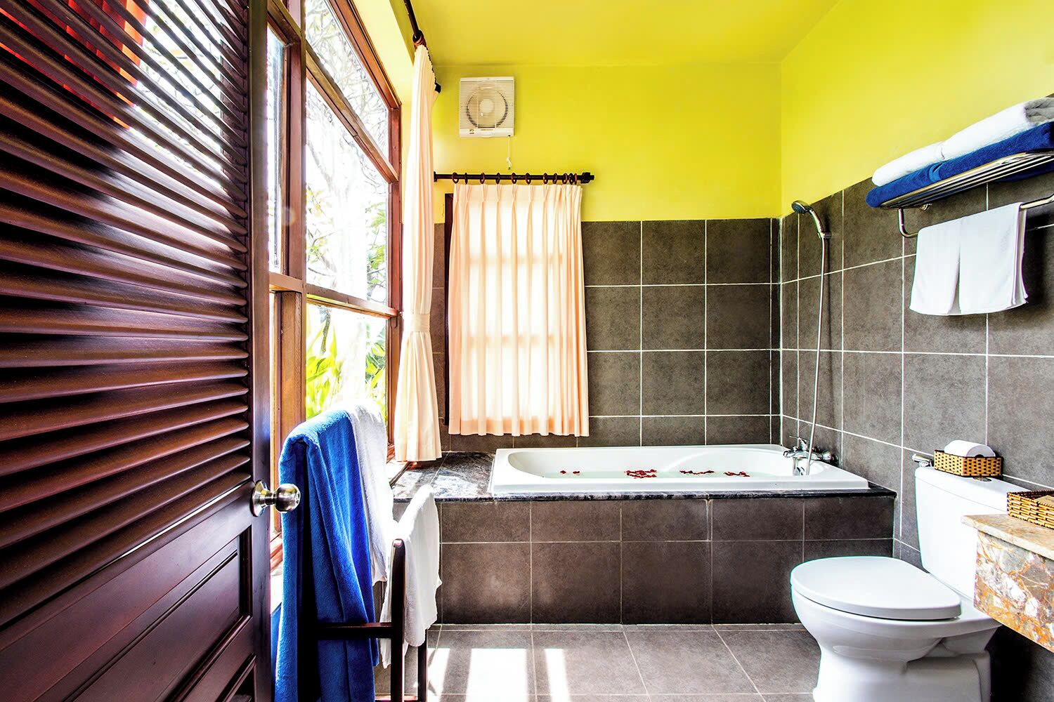 A bathroom with a bathtub, toilet, and window with blinds.