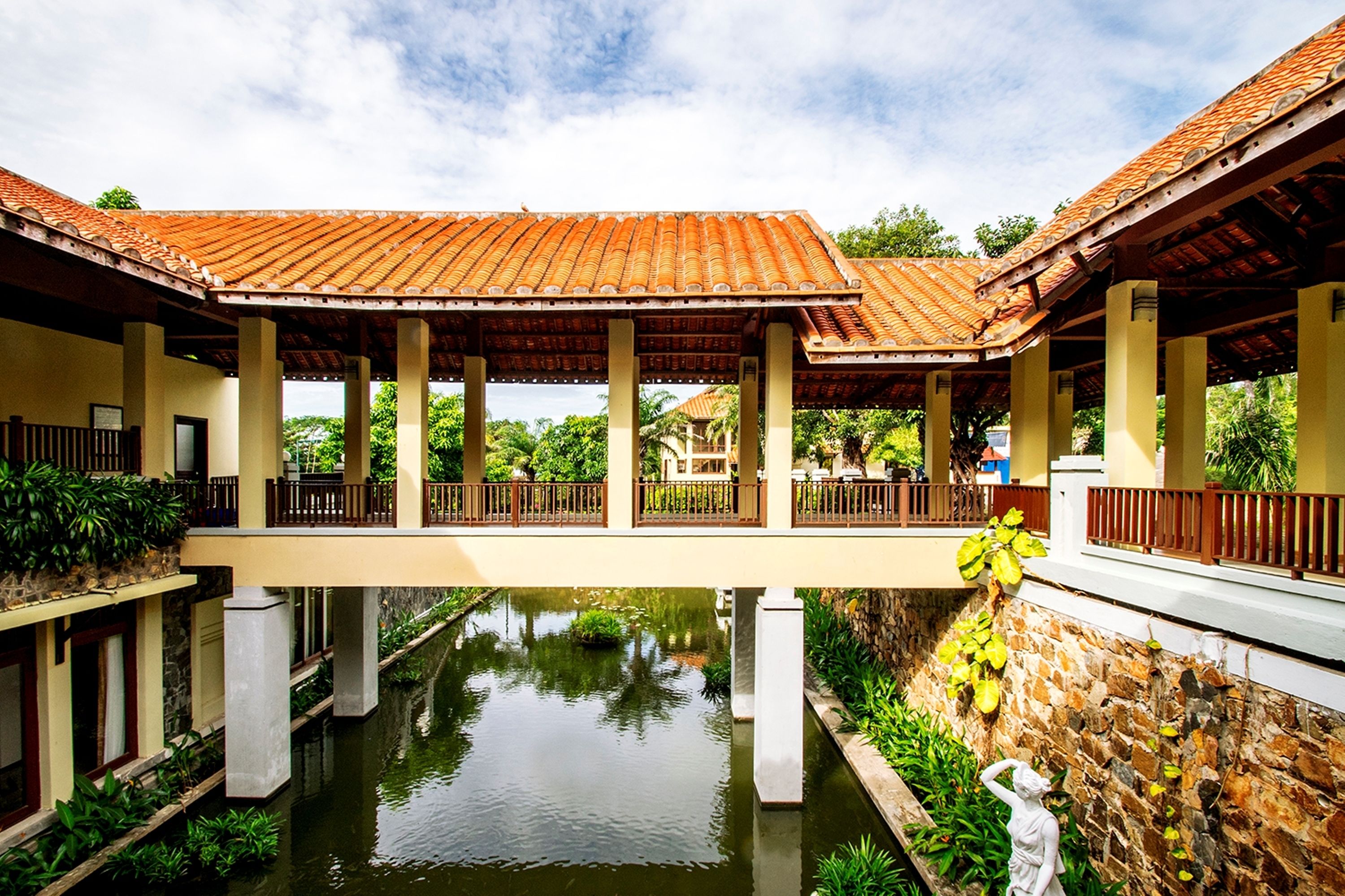 A covered walkway with columns, a water feature, and a statue.