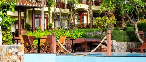 Area piscina con una coppia, l'edificio di un resort tropicale e vegetazione rigogliosa.