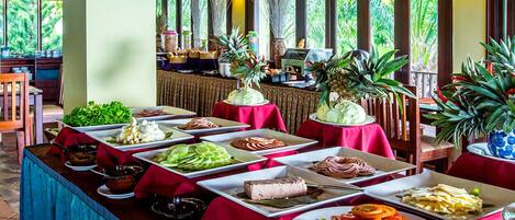 A buffet with various food items and tropical plants.