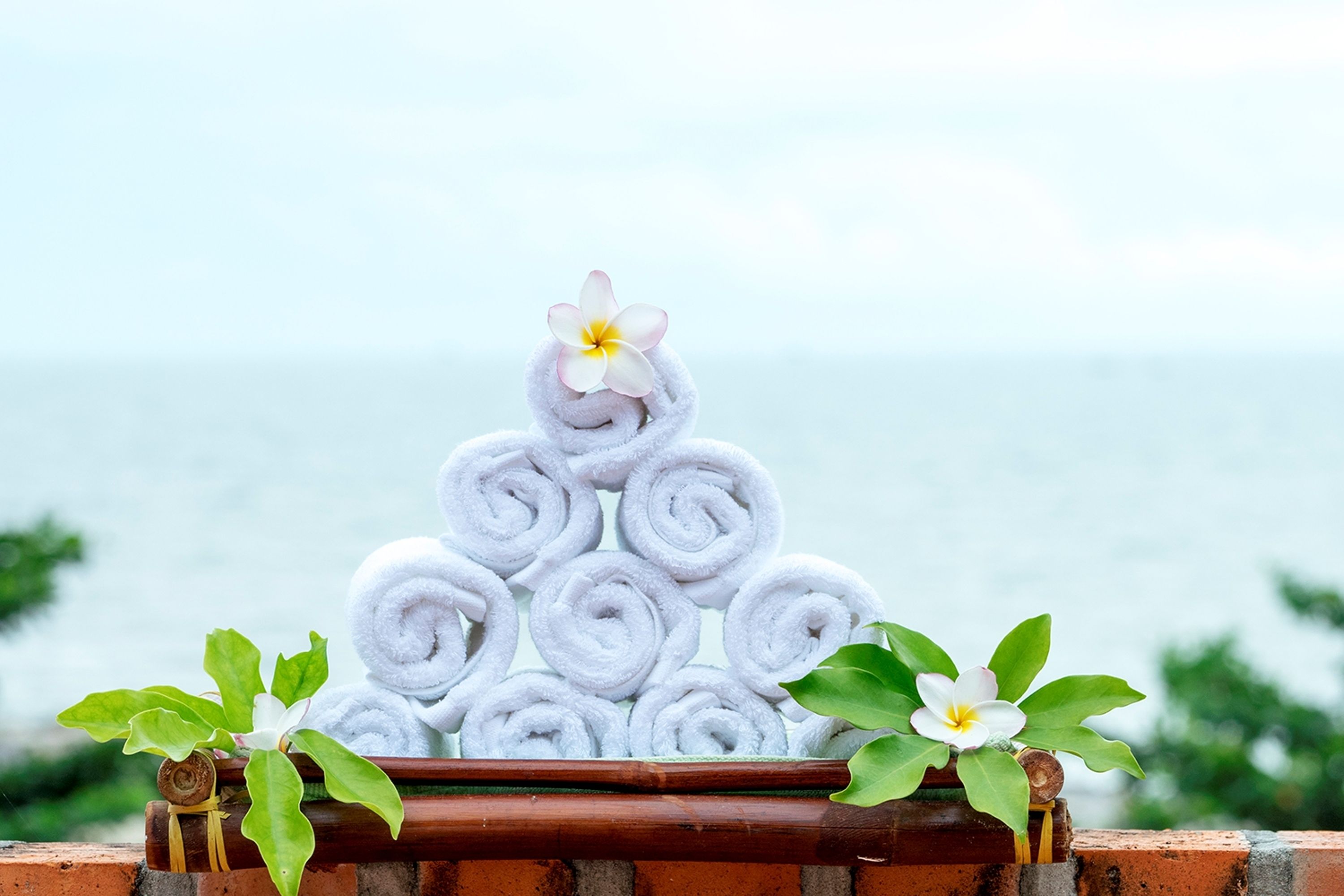 Une pile de serviettes blanches disposées en forme de pyramide sur une étagère en briques, avec une fleur au sommet.