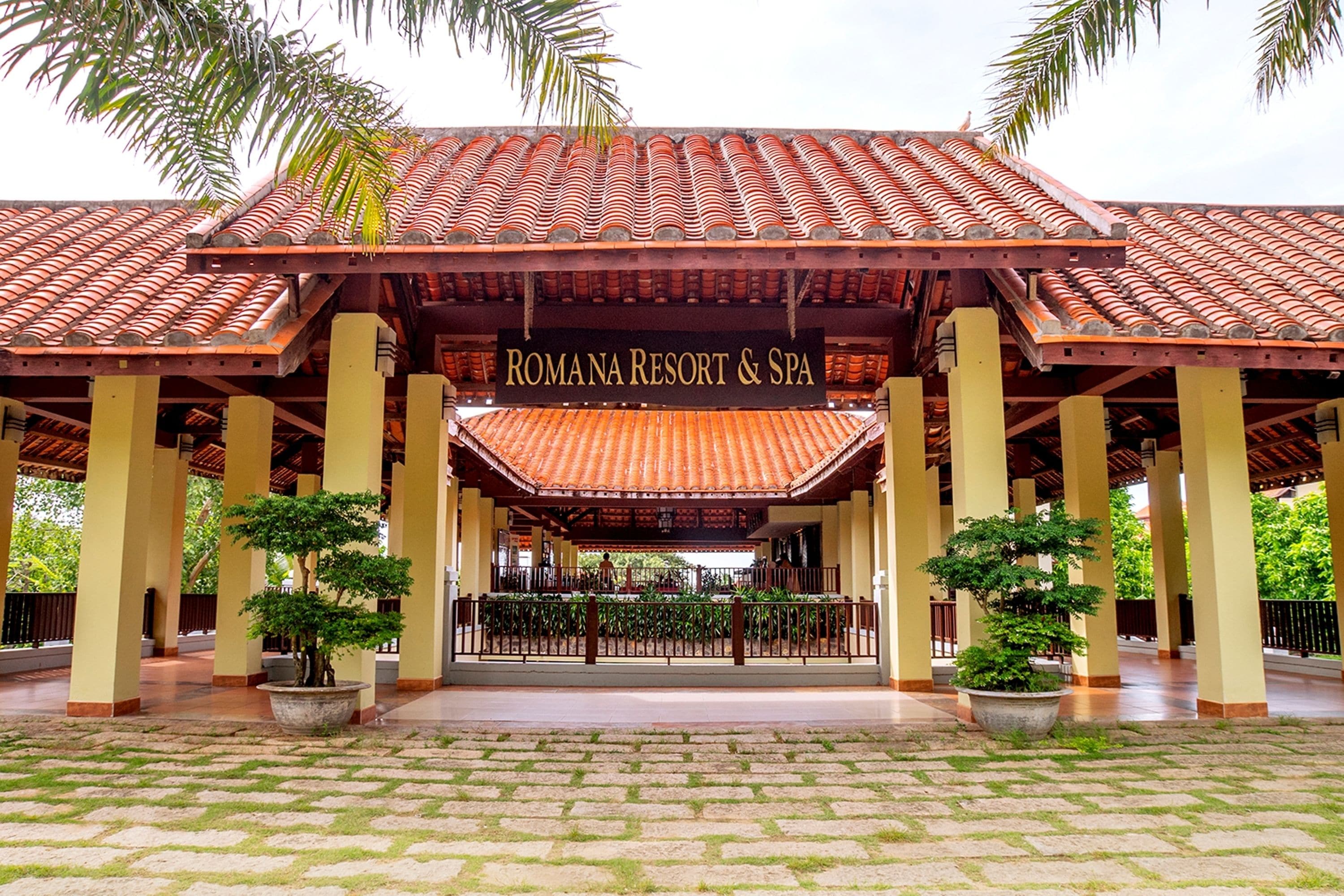 A covered entrance to a resort with a tiled roof and potted plants.