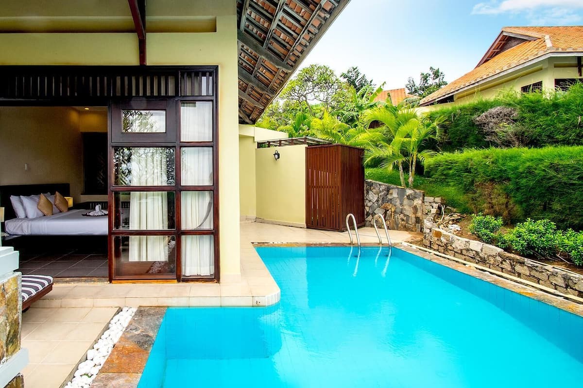 A swimming pool with a glass enclosure, a bed with a view, and a stone wall.