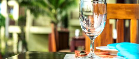 A glass of water on a table with a placemat, a wooden chair, and a blue plate in the background.