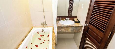 A bathroom with a bathtub filled with rose petals, a sink, and a shower.