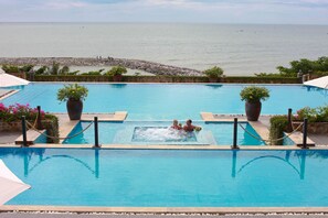 Una piscina con vistas al mar, rodeada de plantas en macetas y un muro de piedra.