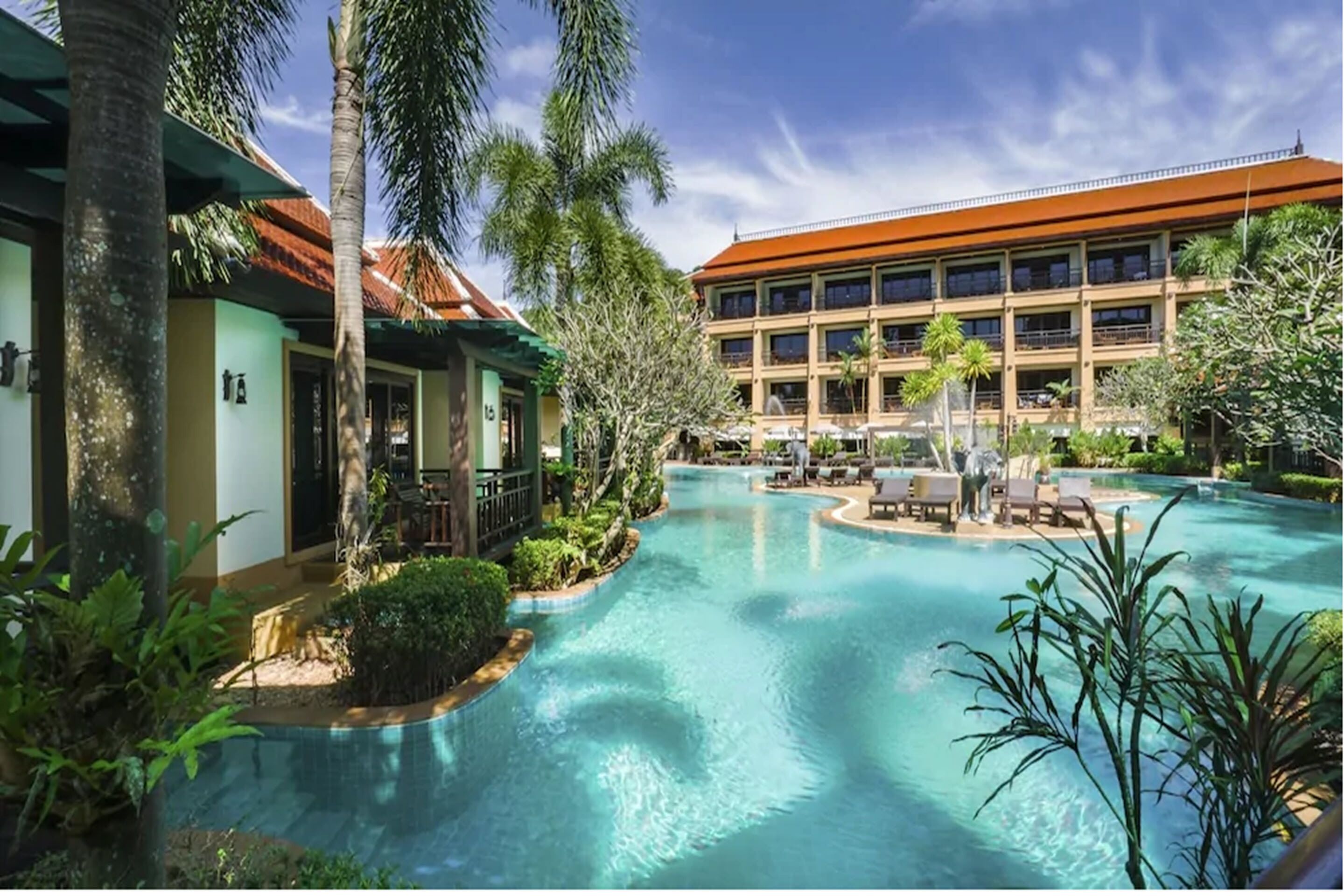 A resort with a central swimming pool surrounded by palm trees and lounge areas.