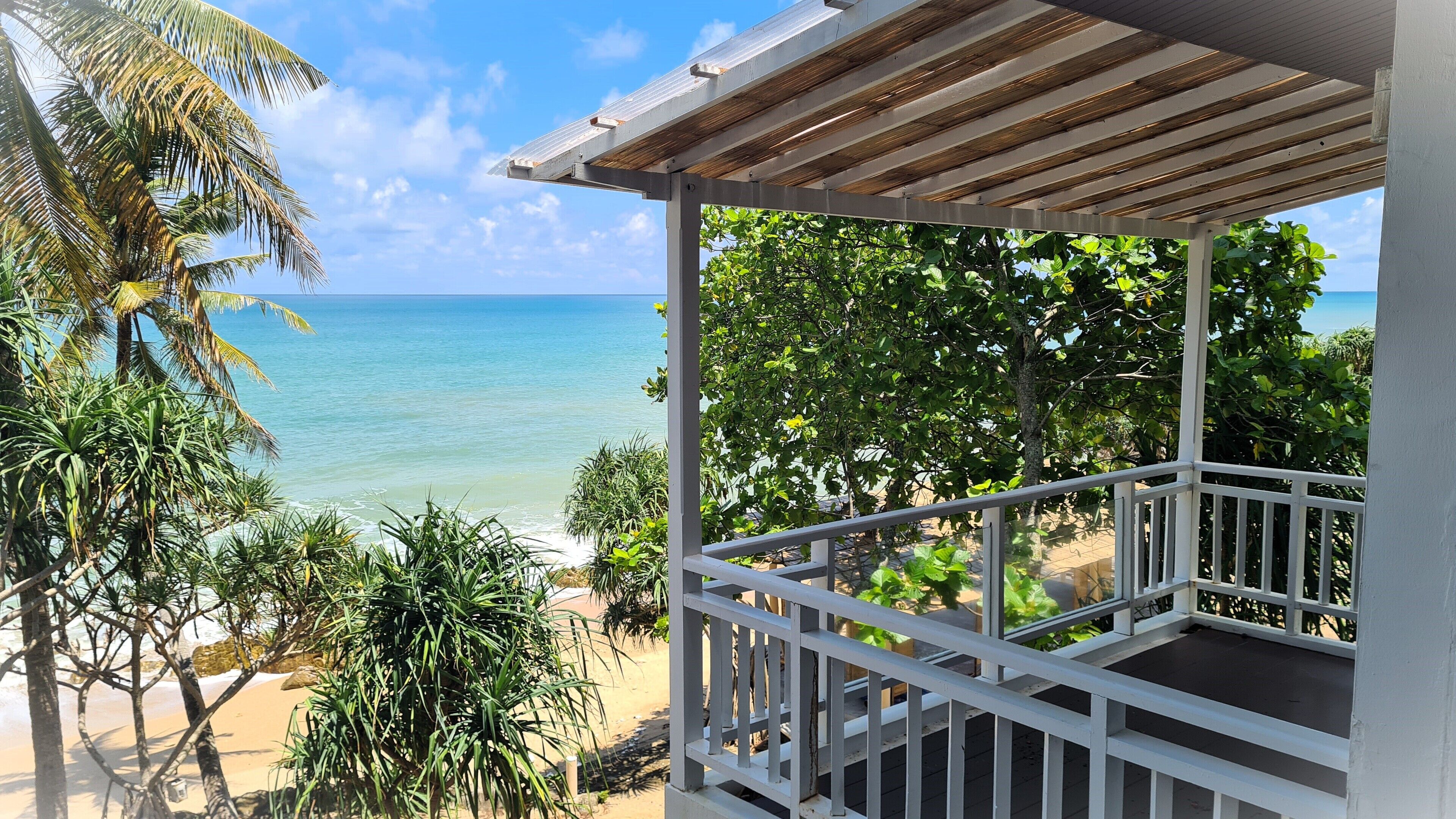 A covered outdoor area with a view of the ocean and tropical vegetation.