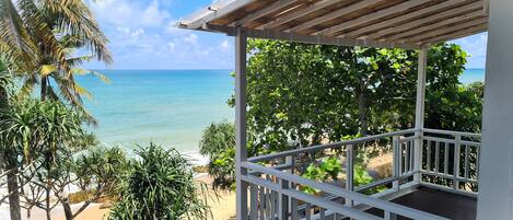 A covered outdoor area with a view of the ocean and tropical vegetation.