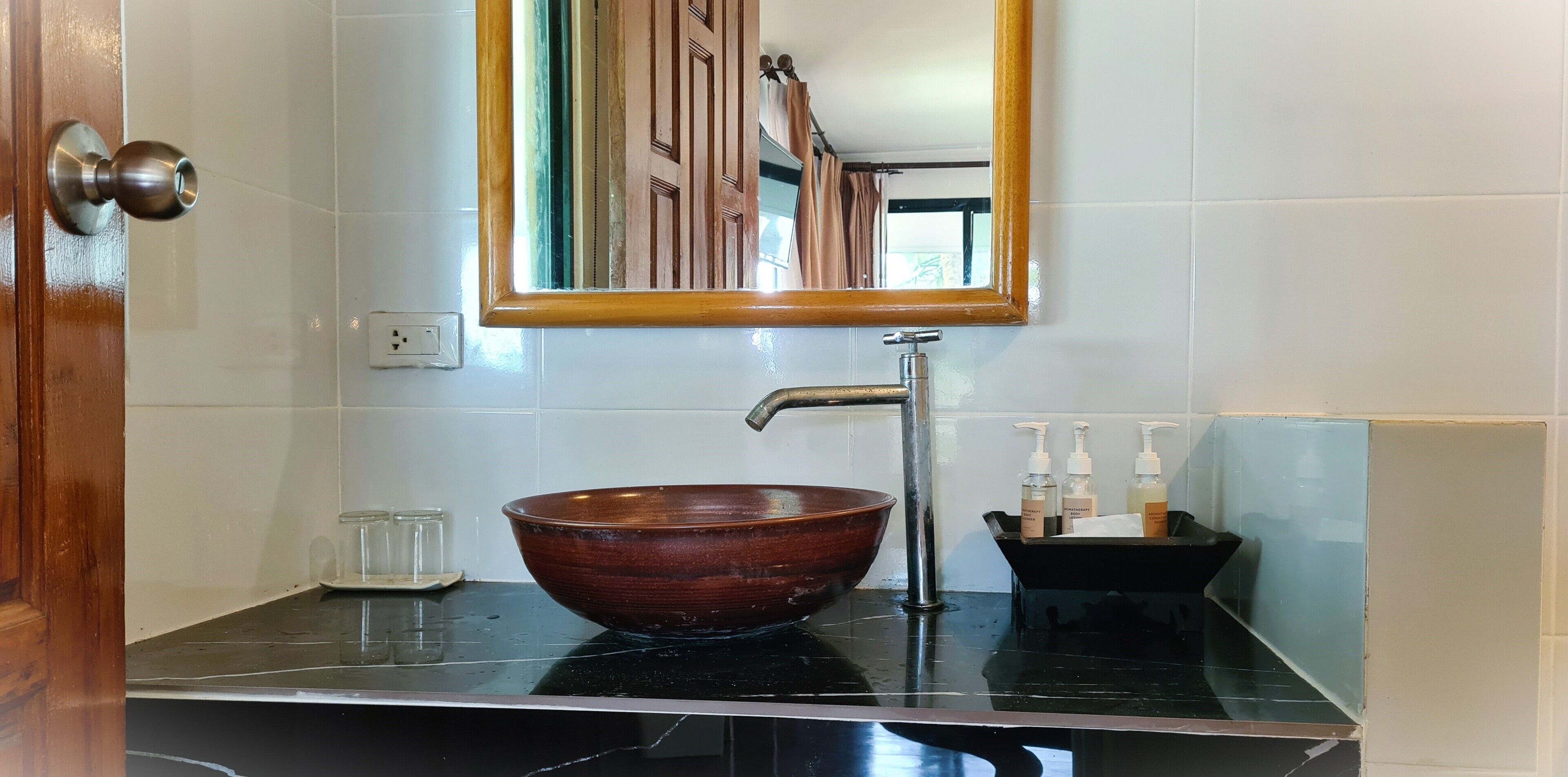 A bathroom with a wooden bowl sink, a mirror, and toiletries on the counter.