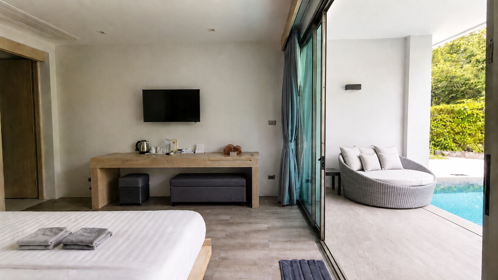 Ein modernes Schlafzimmer mit Bett, Schreibtisch mit Flachbildfernseher und einer Sitzecke mit Blick auf einen Pool.