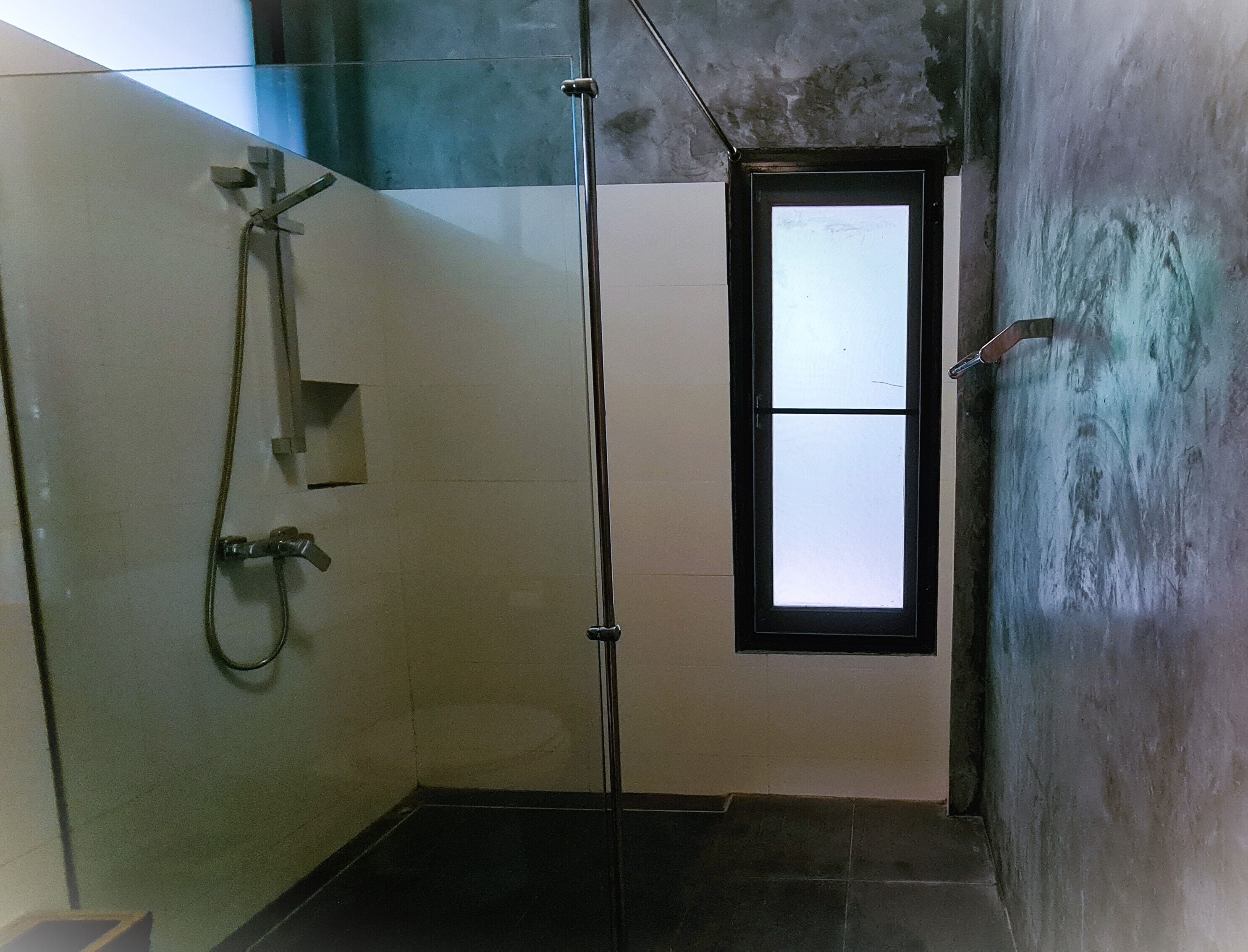 Un área de ducha pequeña y cerrada con separador de vidrio, una ventana y un grifo metálico.