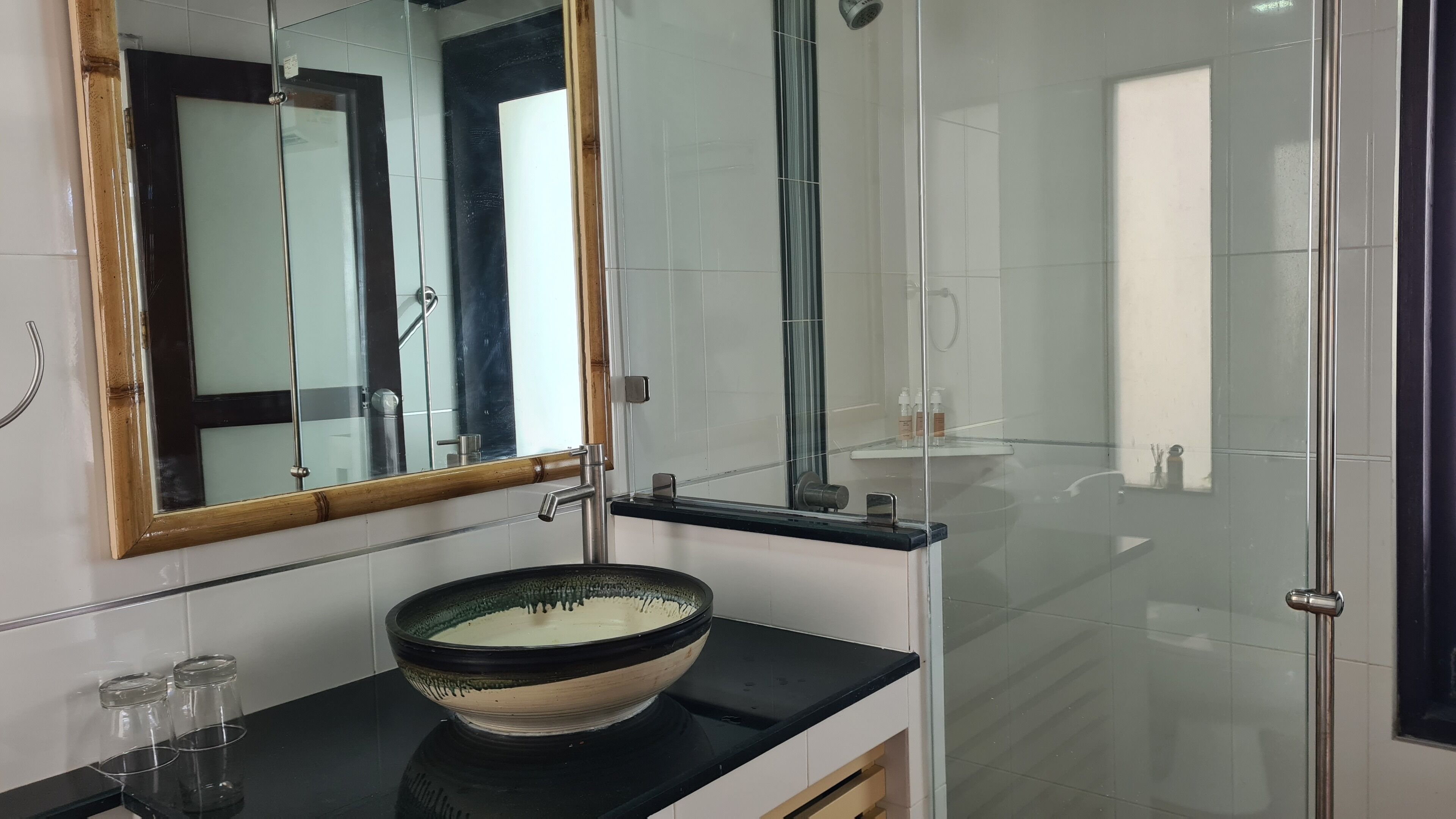 A modern bathroom with a large mirror, a glass shower enclosure, and a black countertop with a ceramic basin.