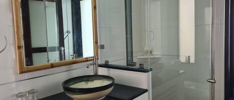 A modern bathroom with a large mirror, a glass shower enclosure, and a black countertop with a ceramic basin.