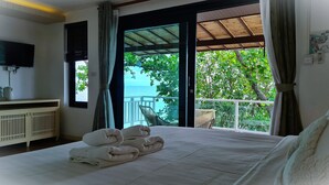 Un dormitorio con cama, televisión, vista al mar y balcón con una silla.