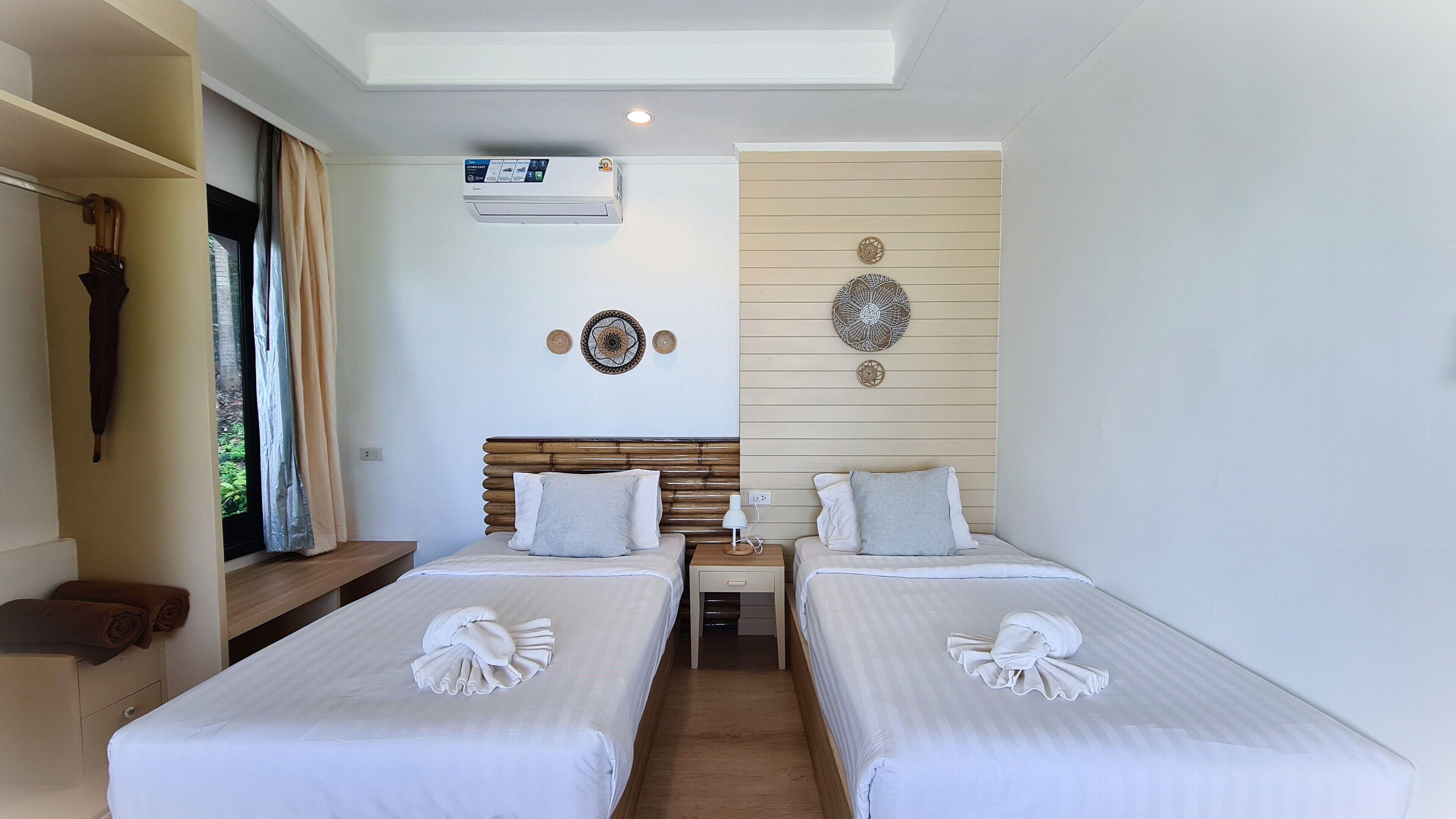 Habitación de hotel con dos camas, ventilador de techo, equipo de aire acondicionado y decoración mural.