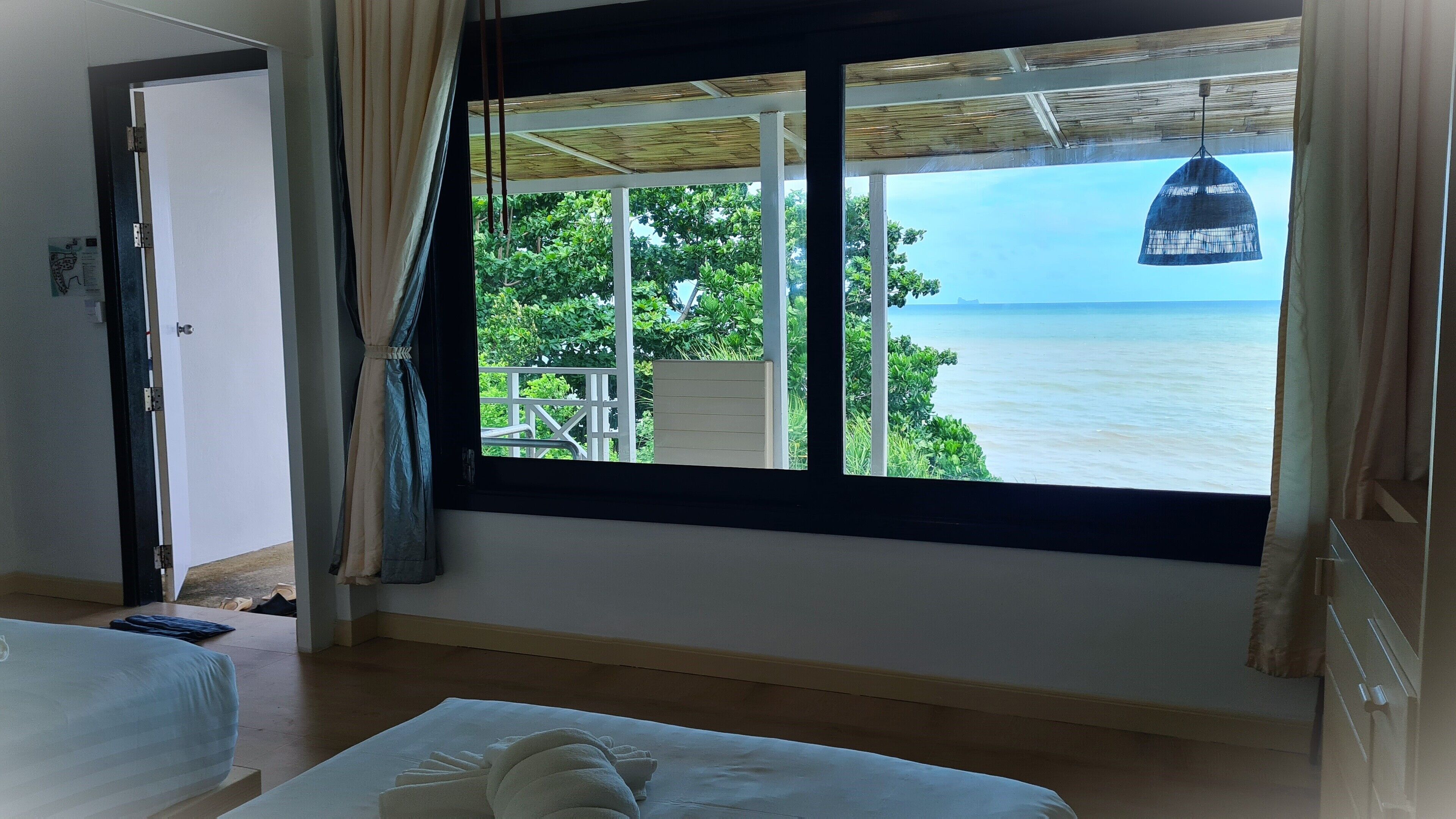 A room with a large window overlooking a body of water, a bed, and a hanging light fixture.