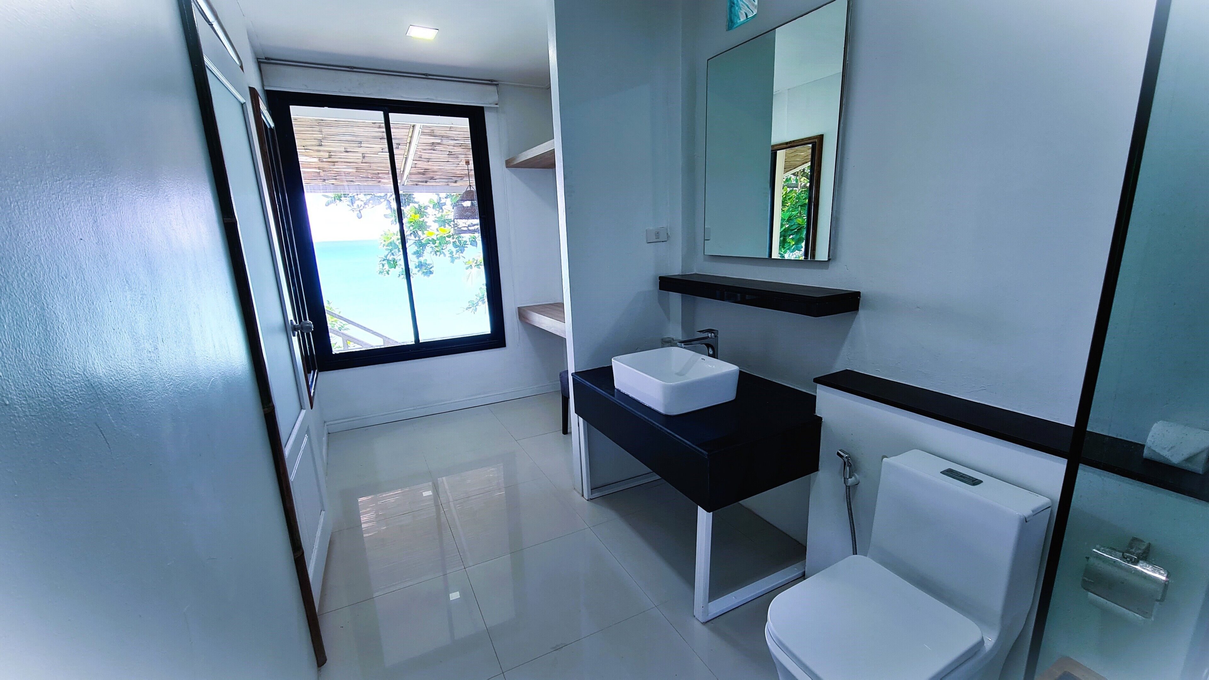 A modern bathroom with a white toilet, a black sink, and a large mirror.