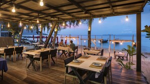 An outdoor dining area with tables and chairs, overlooking a beach and the sea.