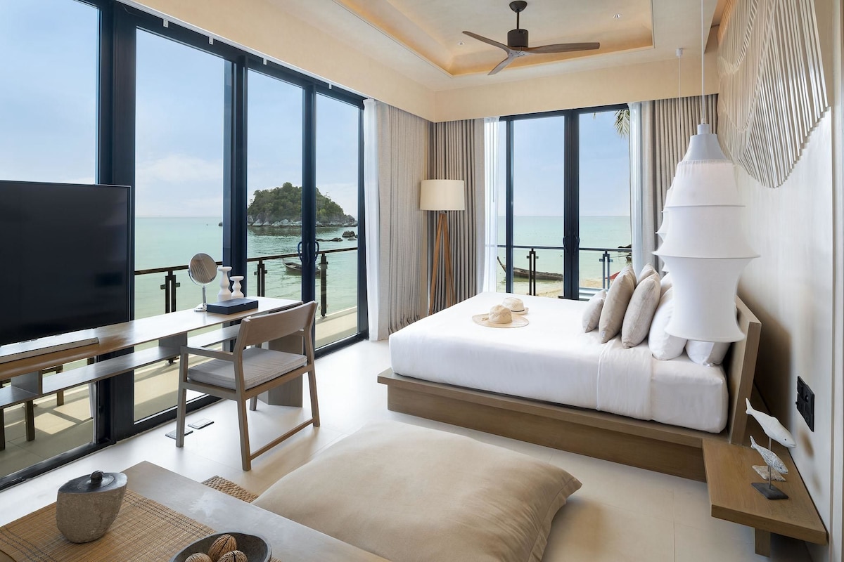 Une chambre d’hôtel avec un lit, un bureau, une chaise, une télévision et une vue sur la mer.