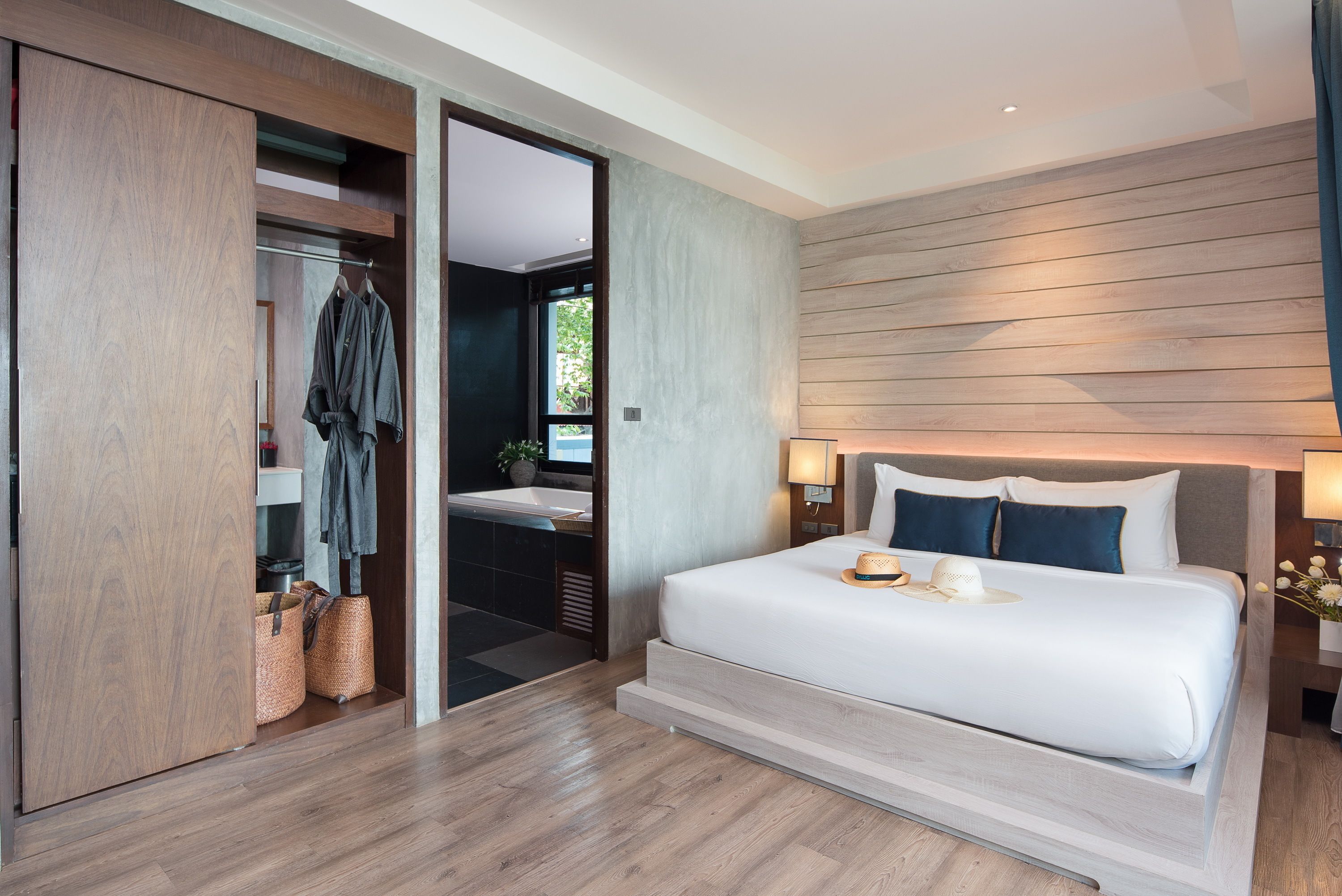 Una habitación de hotel moderna con una cama grande, un vestidor, un baño y vistas al exterior.