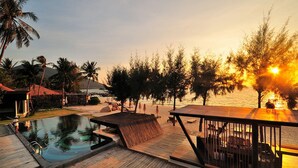 A wooden deck with a pool, outdoor seating, and a view of the sunset over the water. - Idyllic Concept Resort (Koh Lipe)