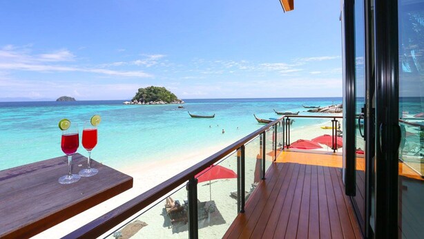 A balcony with a view of a beach and ocean, two drinks on a table, and a wooden deck. - Idyllic Concept Resort (Koh Lipe)