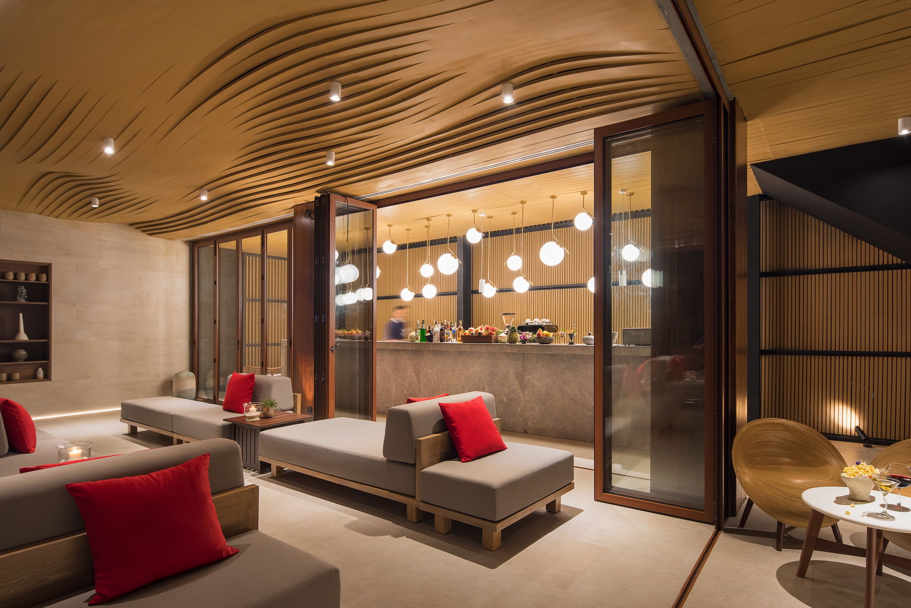 Un interior moderno con techo de madera, una zona de bar y diferentes disposiciones de asientos.