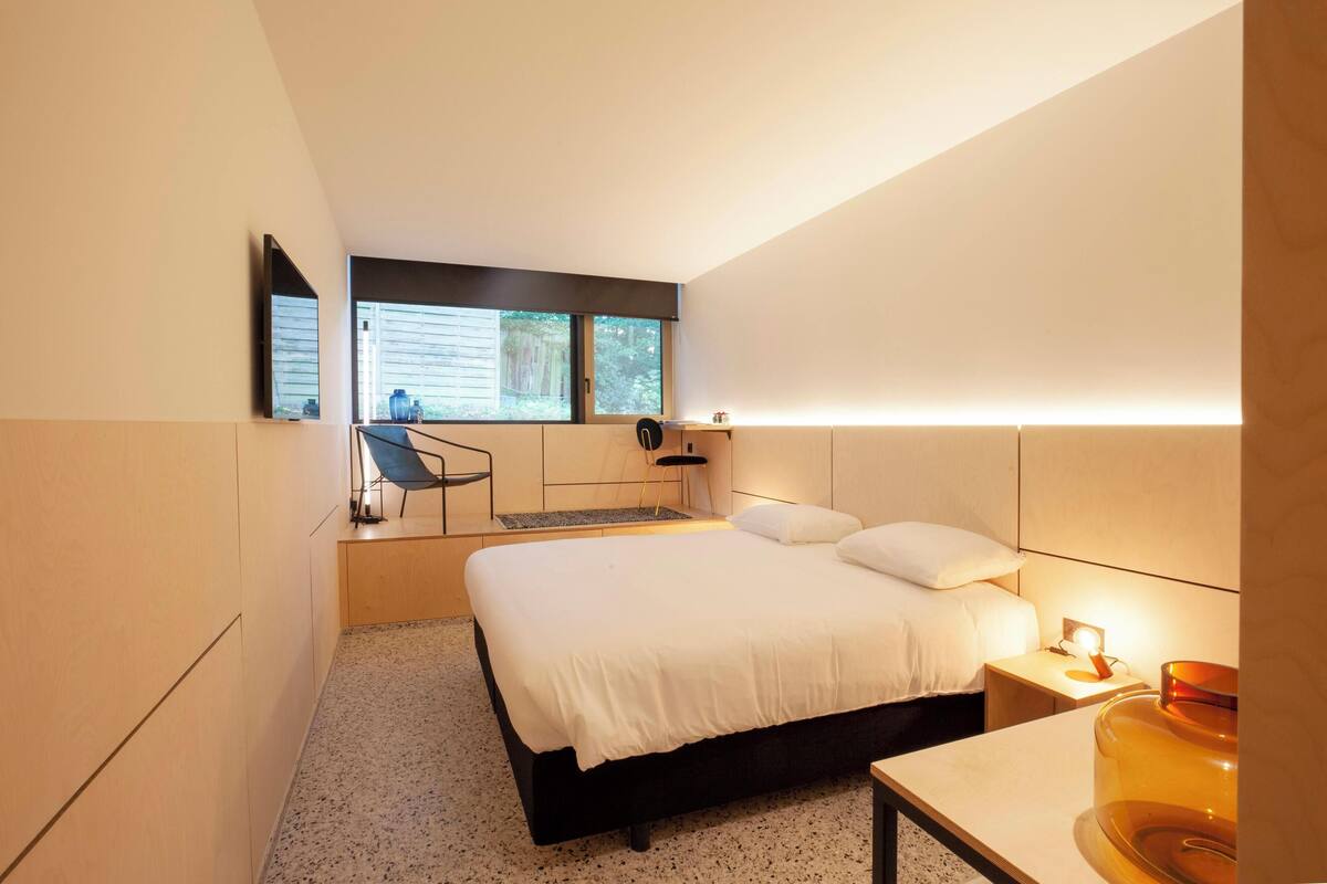 A modern bedroom with a bed, bedside table, lamp, and a window with a view.