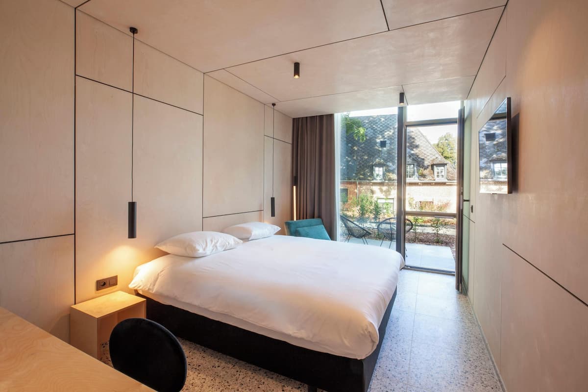 A modern hotel room with a large bed, a desk, and a view of the outside.