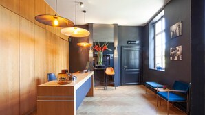 A reception area with a wooden reception desk, two blue chairs, a blue sofa, and a large window. - Hotel The Lodge Heverlee (Leuven)