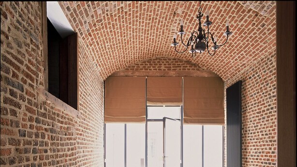 A bedroom with a brick wall, a bed with white linens, a bedside lamp, and a chandelier. - Hotel The Lodge Heverlee (Leuven)
