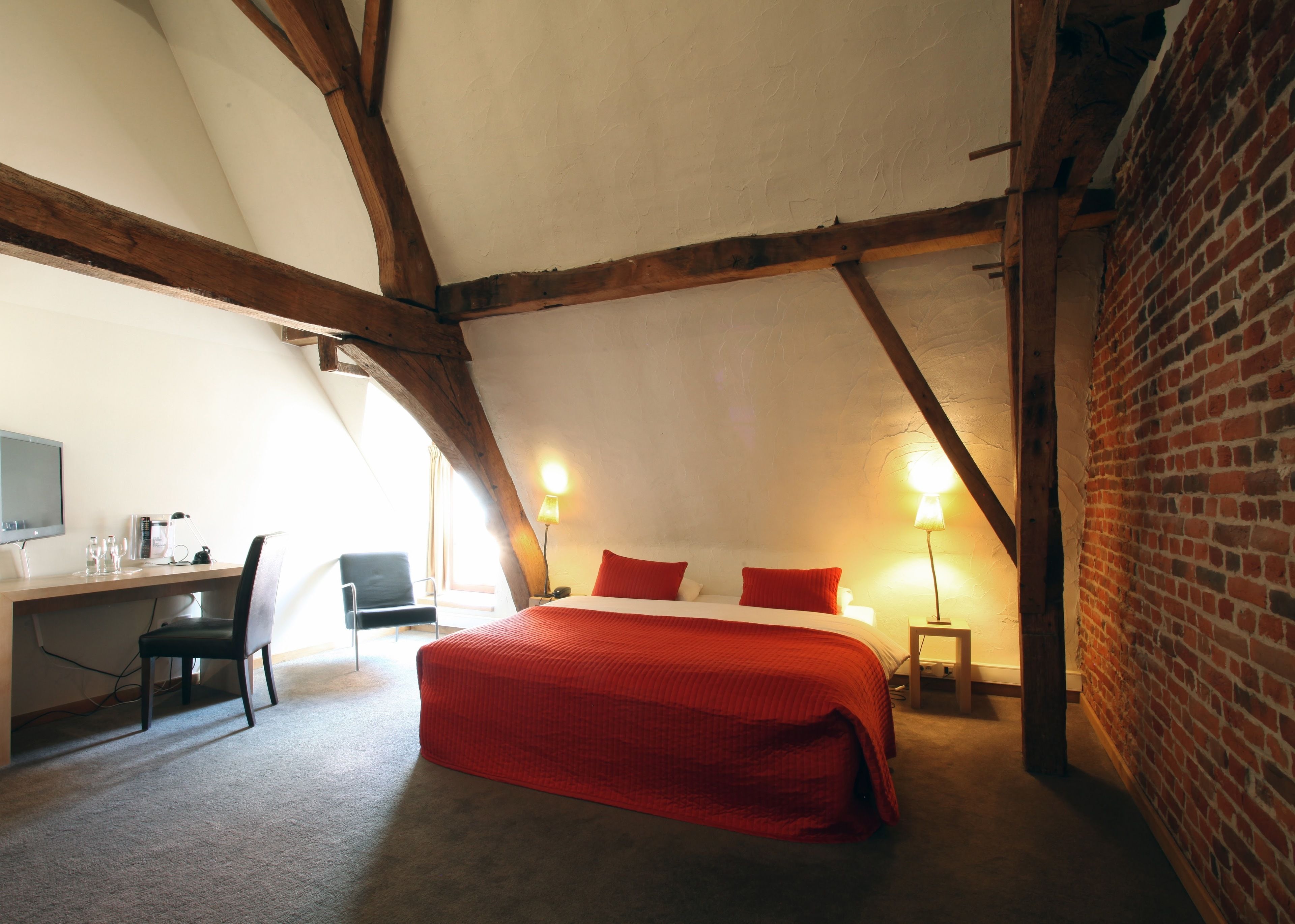 A bedroom with a large bed, a desk with a chair, and a TV.