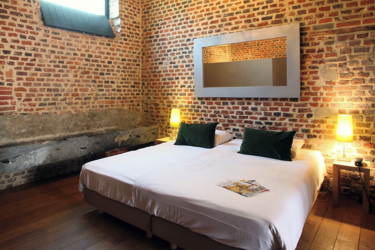 A room with a brick wall, a bed with green pillows, and two bedside lamps.