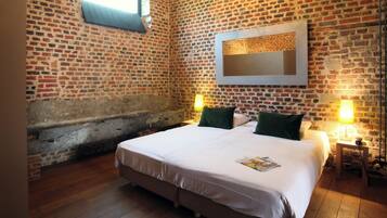 Una habitación con pared de ladrillo, cama con almohadas verdes y dos lámparas de noche.