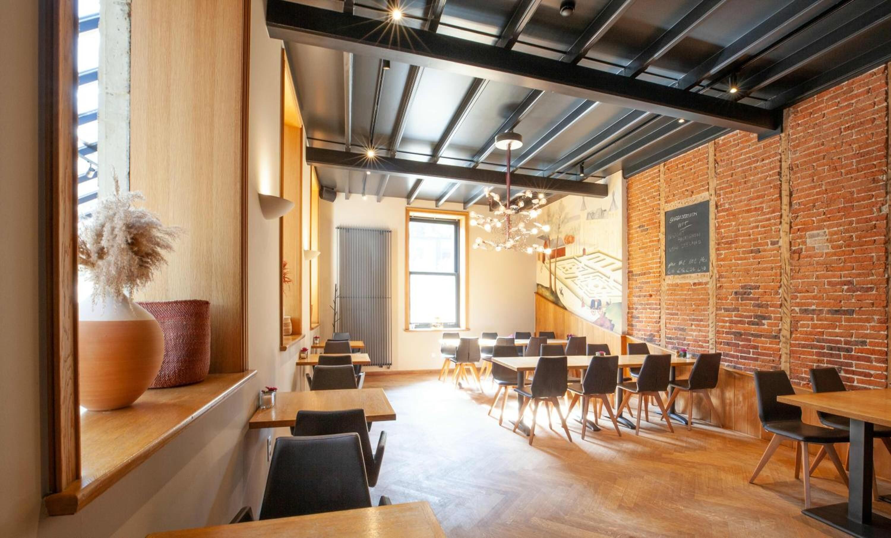 Un comedor moderno con mesas y sillas de madera, una pared de ladrillo y un ventanal grande.