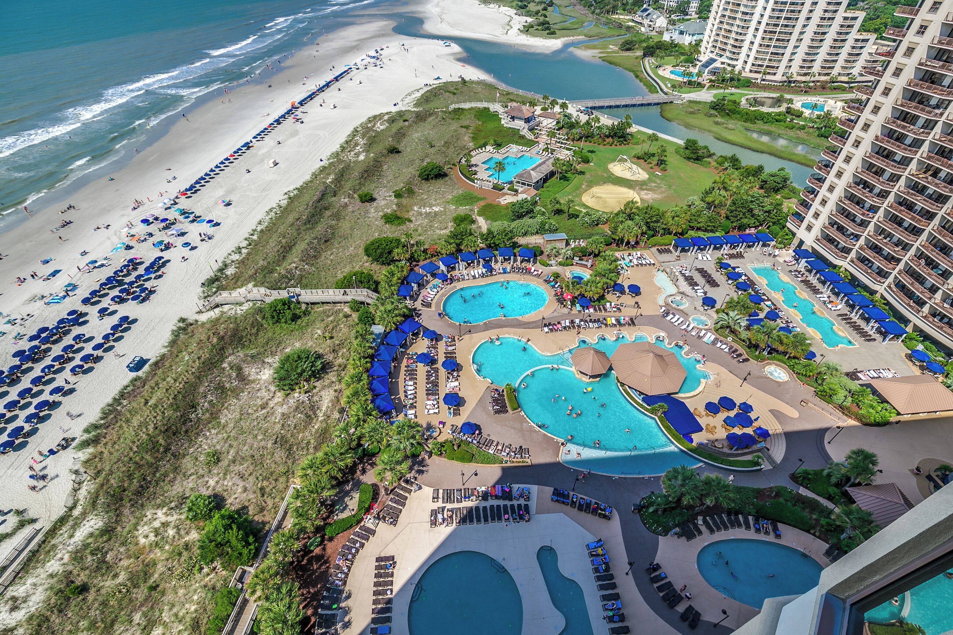 An aerial view of a resort with multiple swimming pools, a beach, and a golf course.