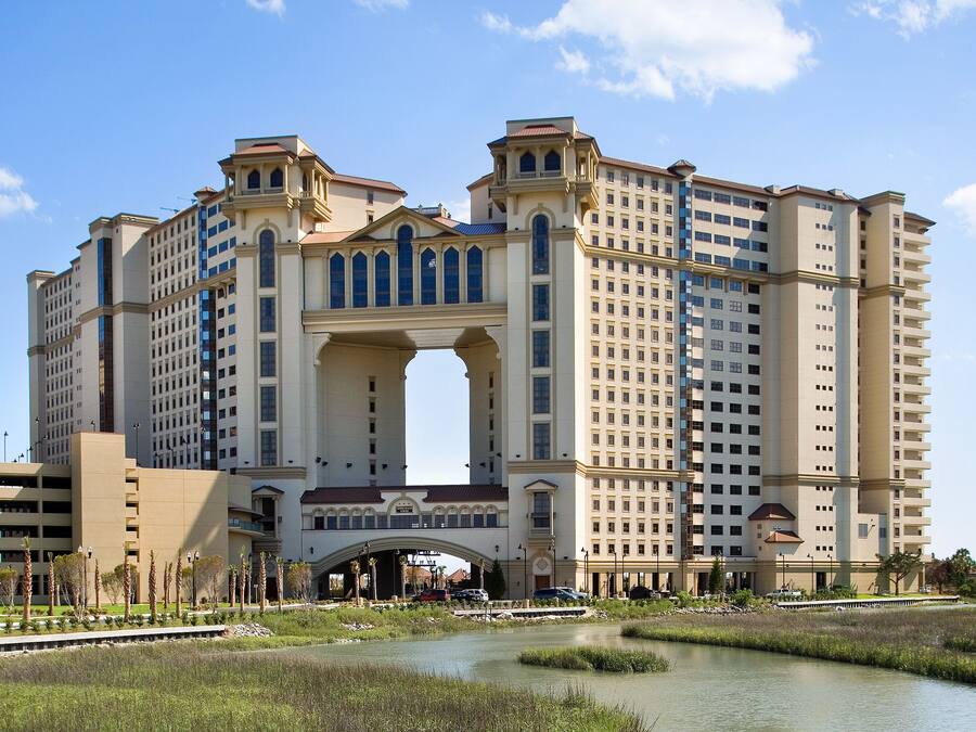 A large hotel with a central archway, multiple floors, and a parking area in front.