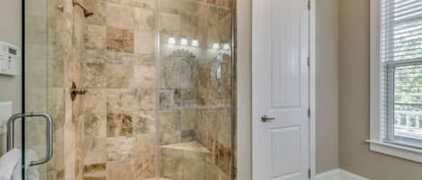 A shower with a glass door, a white door next to it, and a window with blinds.