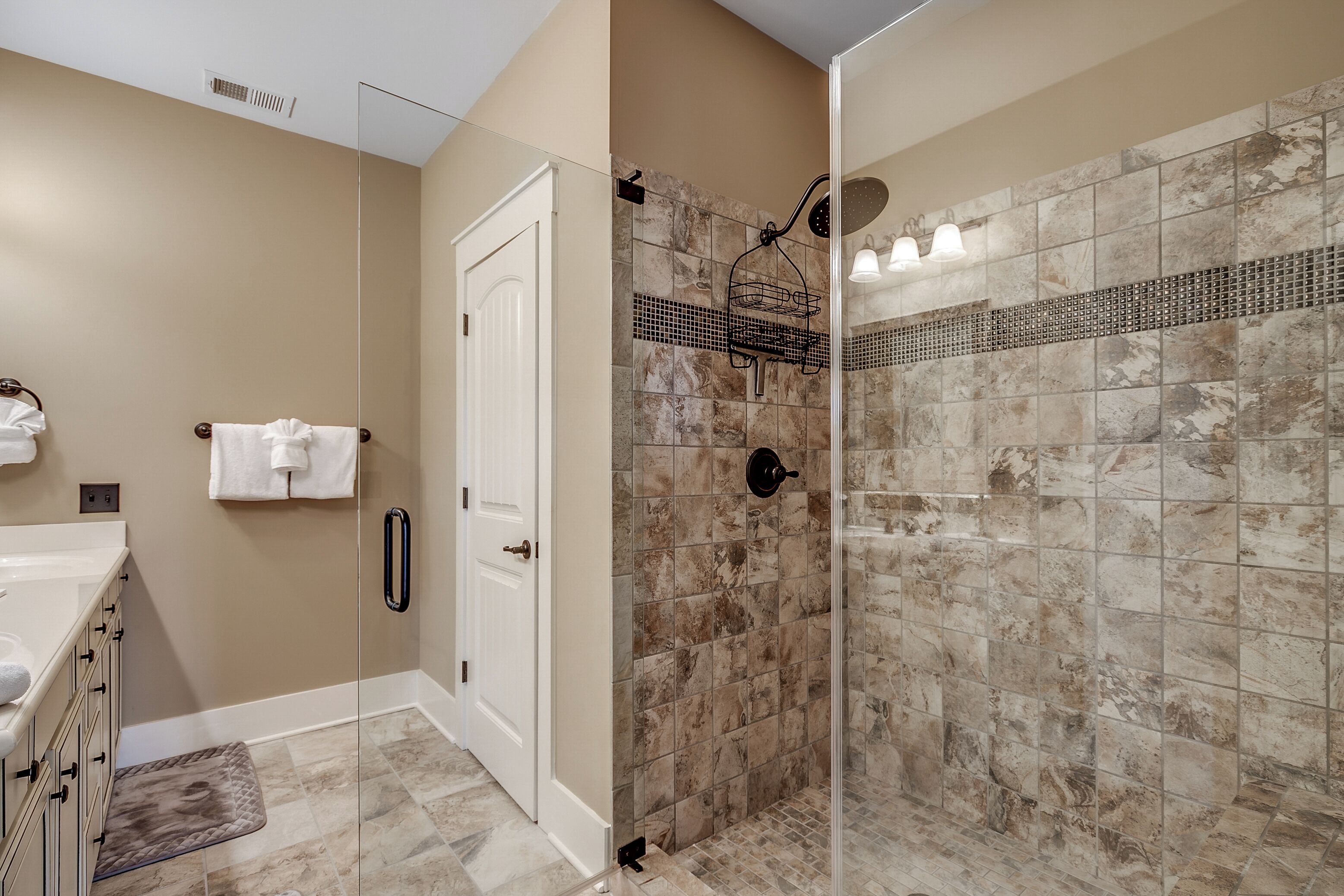 A bathroom with a walk-in shower, beige walls, and a tiled floor.