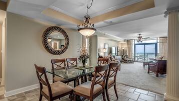 A dining area with a glass table and wooden chairs, a chandelier, and a large mirror on the wall.