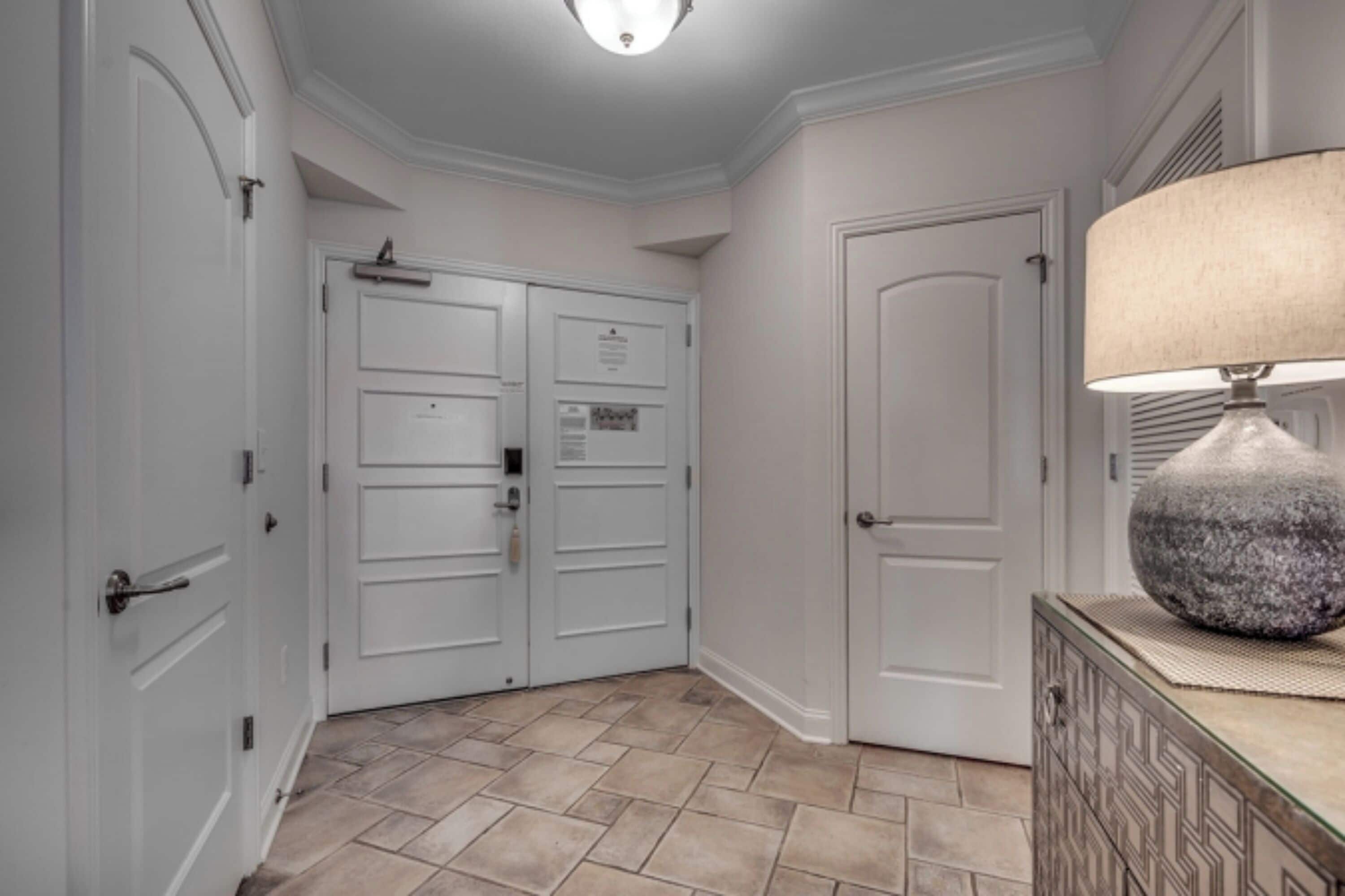 A hallway with double doors, a lamp, and a patterned cabinet.