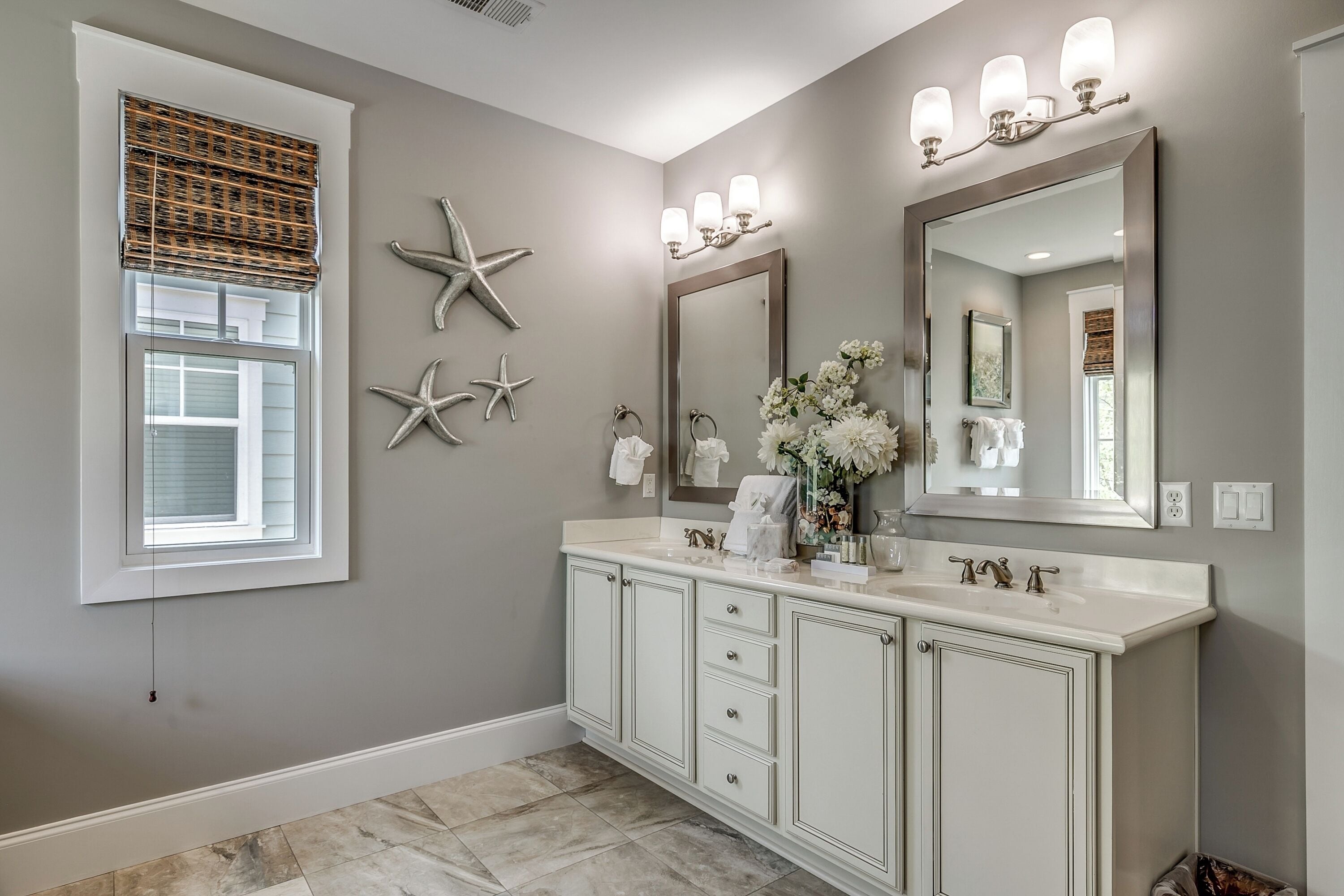 A bathroom with a vanity, a large mirror, wall sconces, and decorative starfish.
