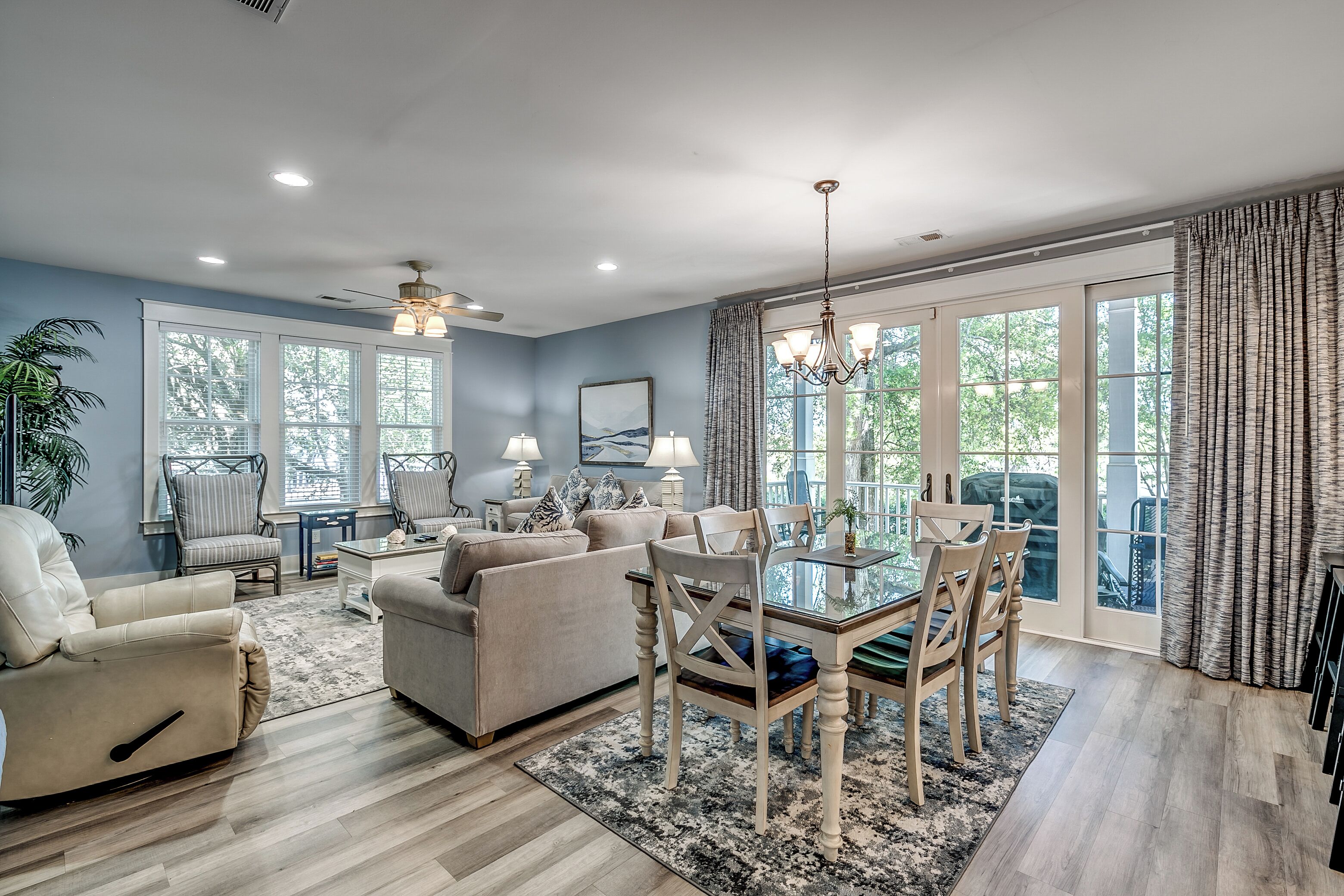 A spacious living room with a dining area, large windows, and a ceiling fan.