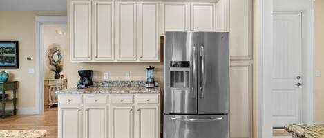 A kitchen with white cabinetry, a stainless steel refrigerator, and a granite countertop.