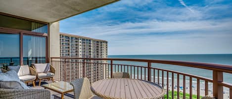 Een balkon met rieten meubilair, een ronde tafel en uitzicht op het strand.