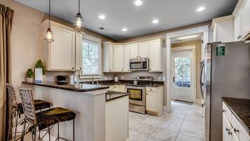 A modern kitchen with white cabinetry, stainless steel appliances, and a central island with bar stools.