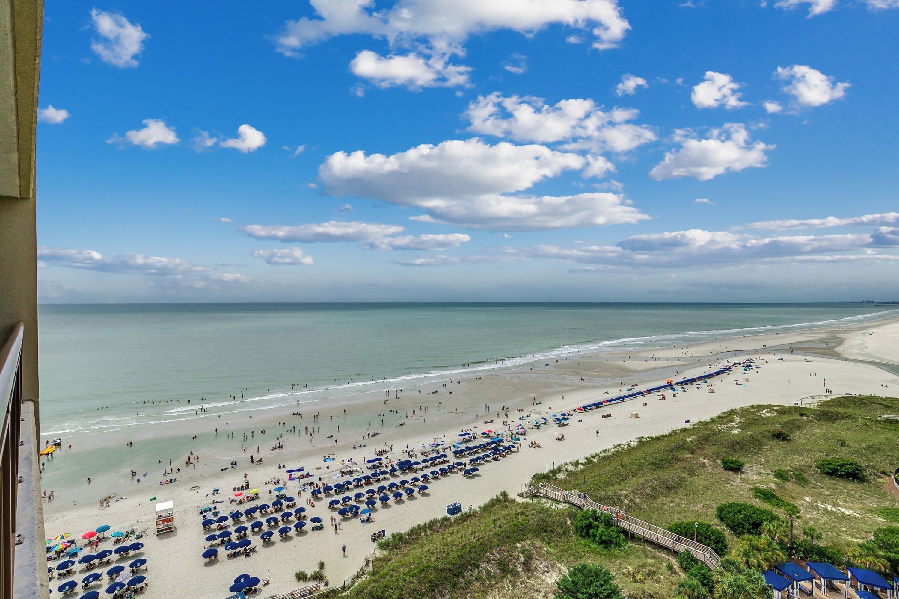 A beach with umbrellas and people, a clear sky, and a view of the ocean.
